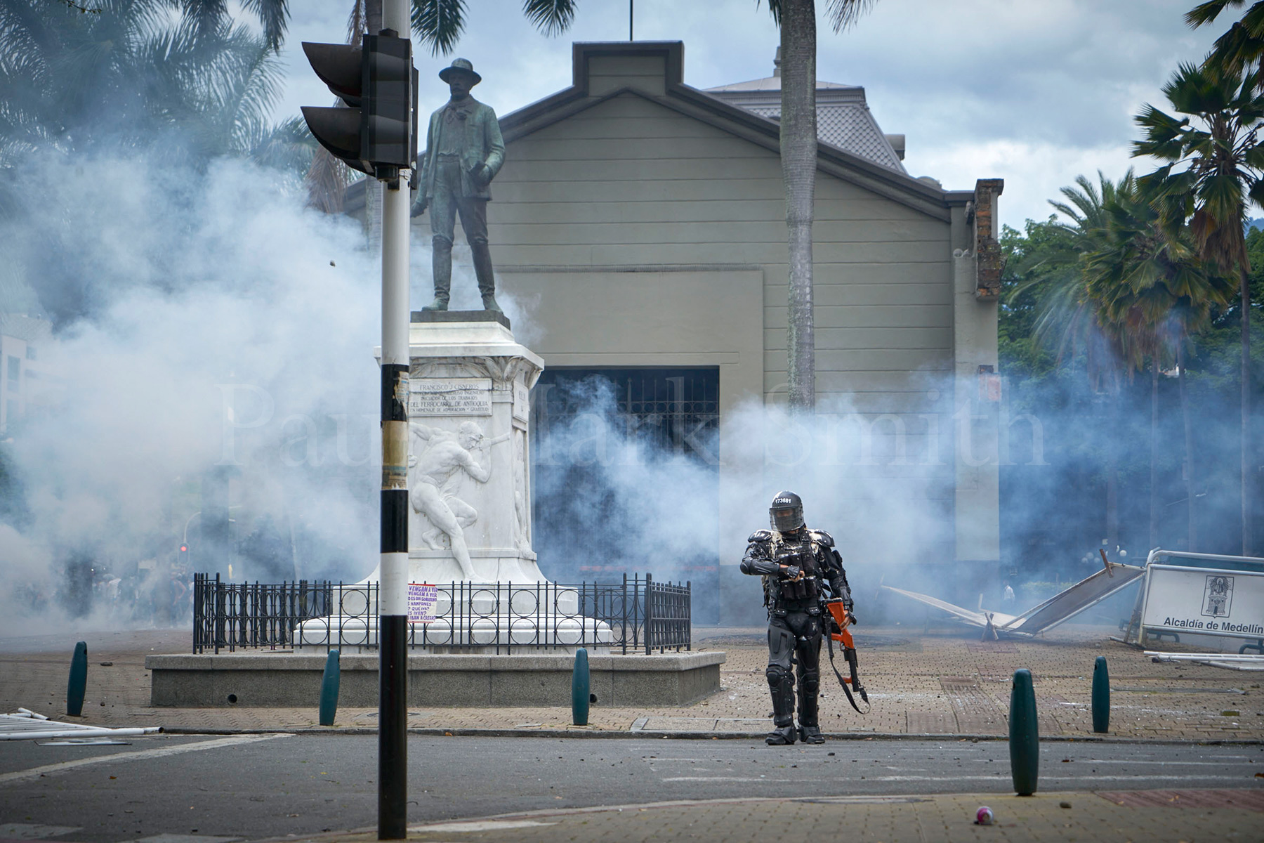 A riot policeman covered in white paint walks and make to reload his weapon in clouds of gas