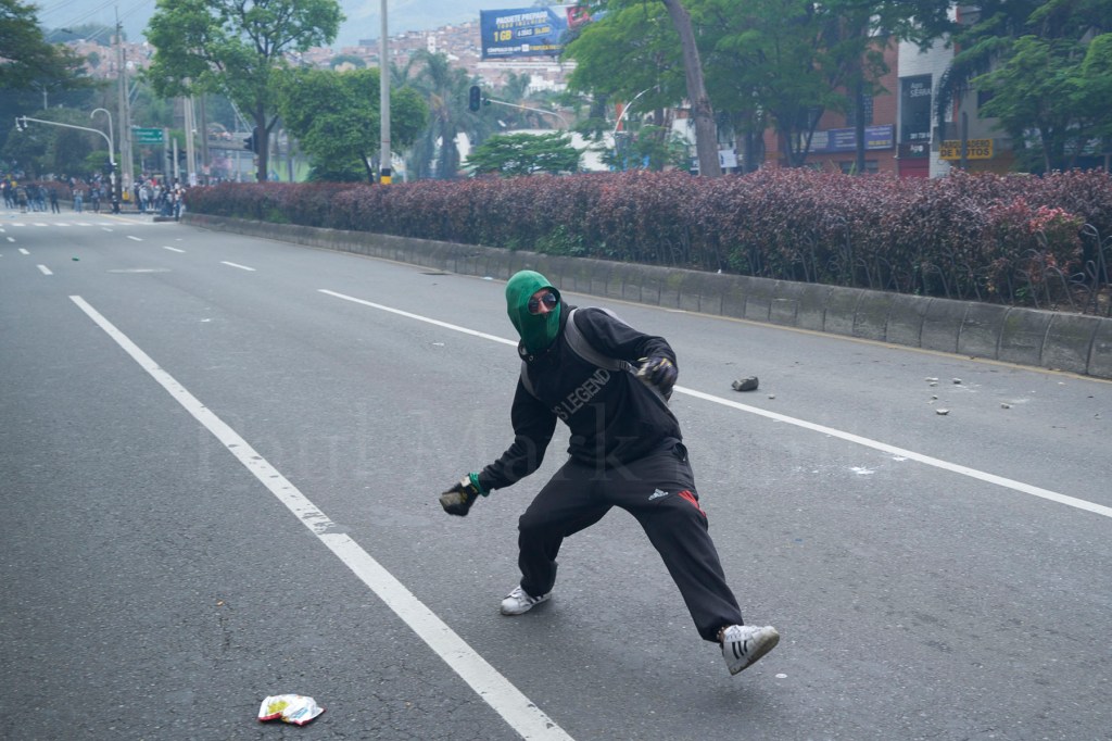 A hooded protester throws a stone towards police