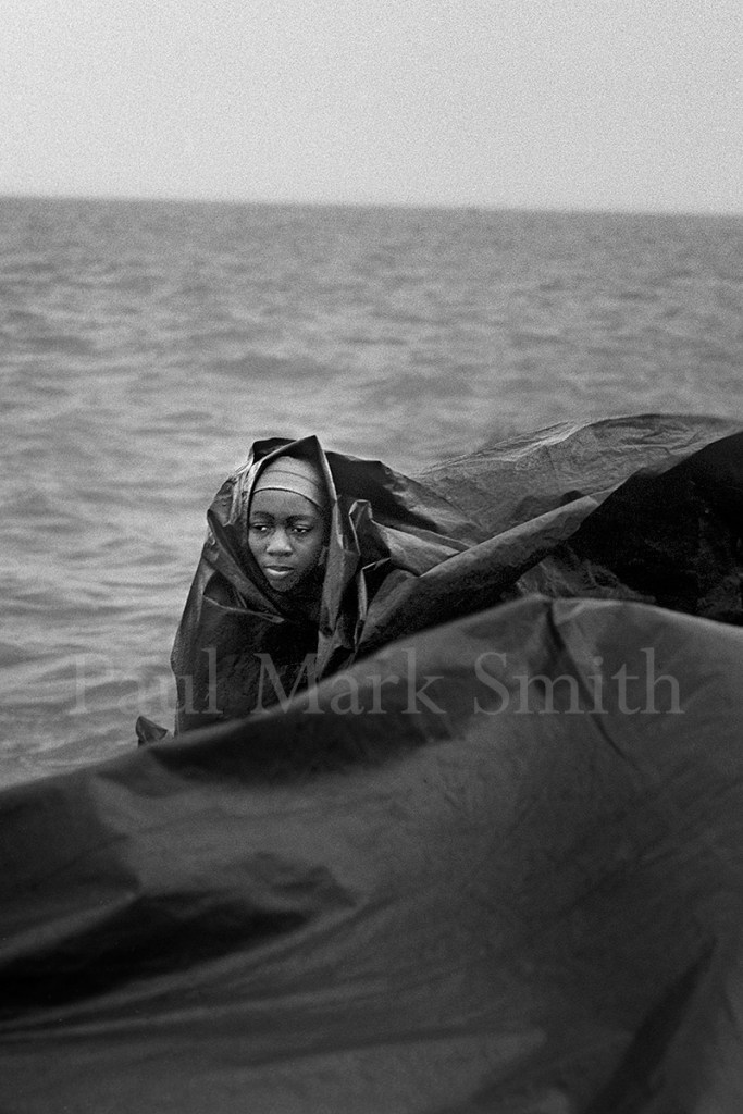 A young woman wrapped in a plastic sheet crosses turbulent water