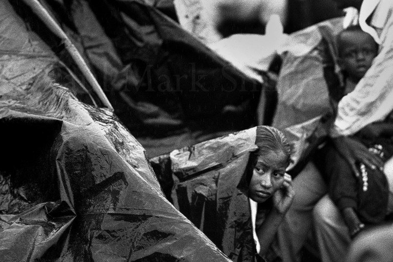 A woman look out from a plastic sheet as she shelters from the water whilst crossing a gulf