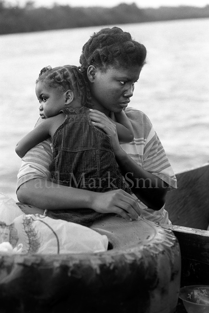 A mother with her girl child in a wooden boat that passes along a river