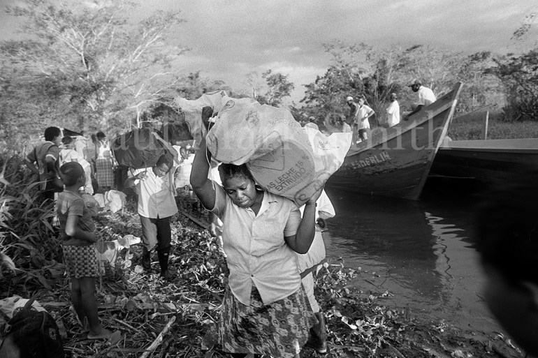 A woman carries her possessions on her shoulder as wooden boats arrive and people disembark