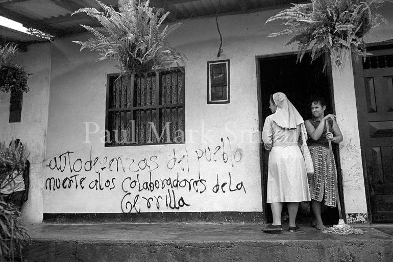 A nun speaks with a woman with a broom as they look at paramilitary graffiti on the woman's home