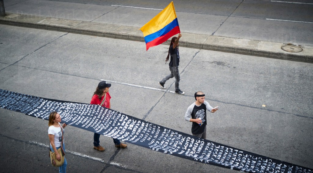 A long banner with list of murdered activists and man with Colombian flag