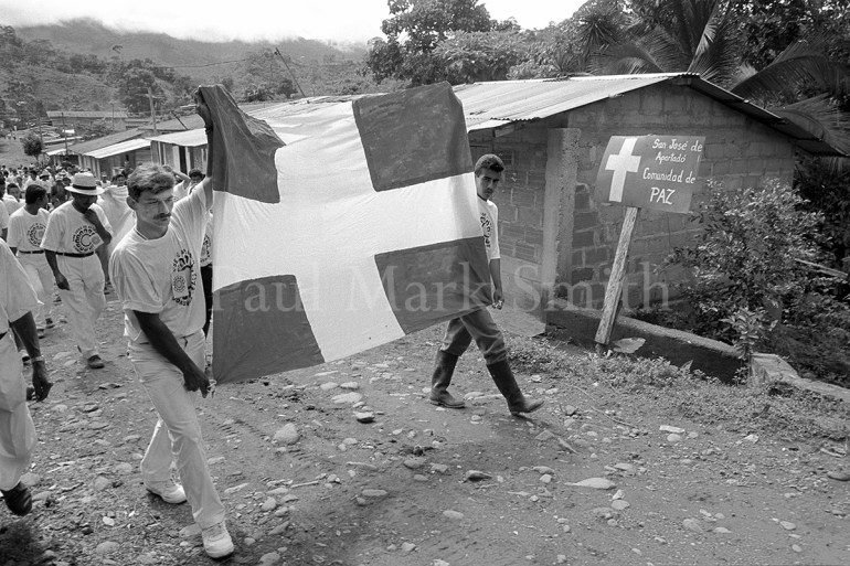 A march of farmers, who hold a flag with a white cross, through a small Colombian village.