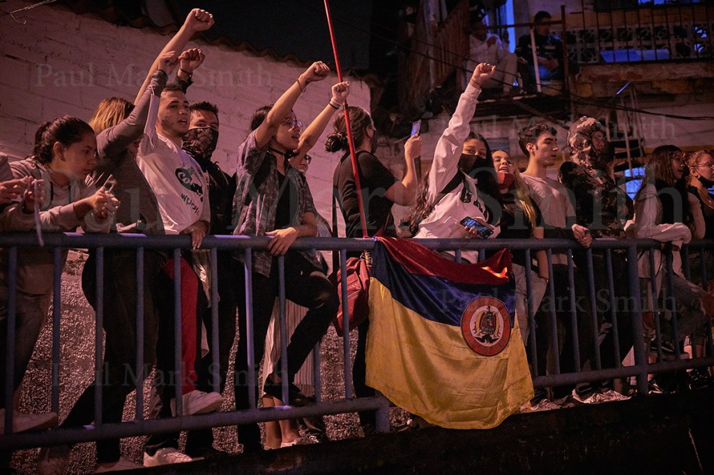 Fists in the air, youths chant anti-government slogans with an inverted Colombian flags