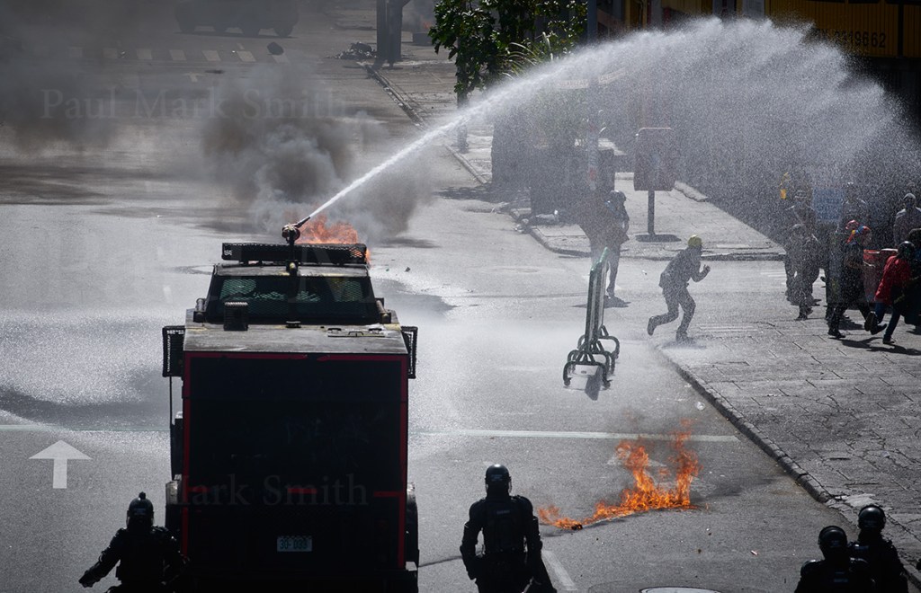 Protester with sheild and police water canon