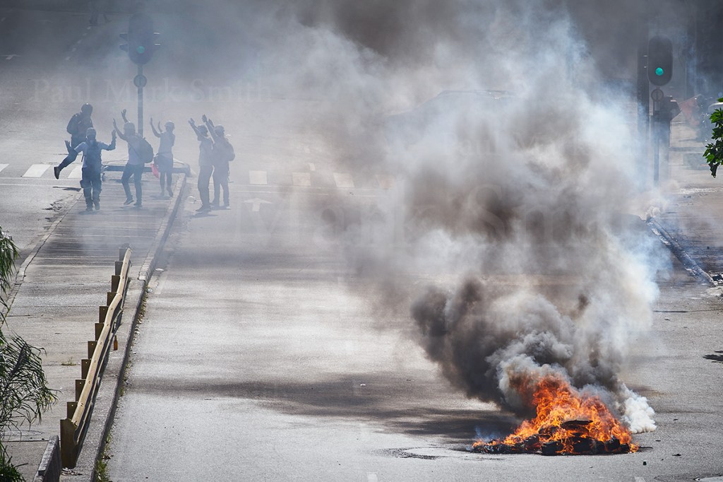 Burning barricade and paramedics with their arms held aloft