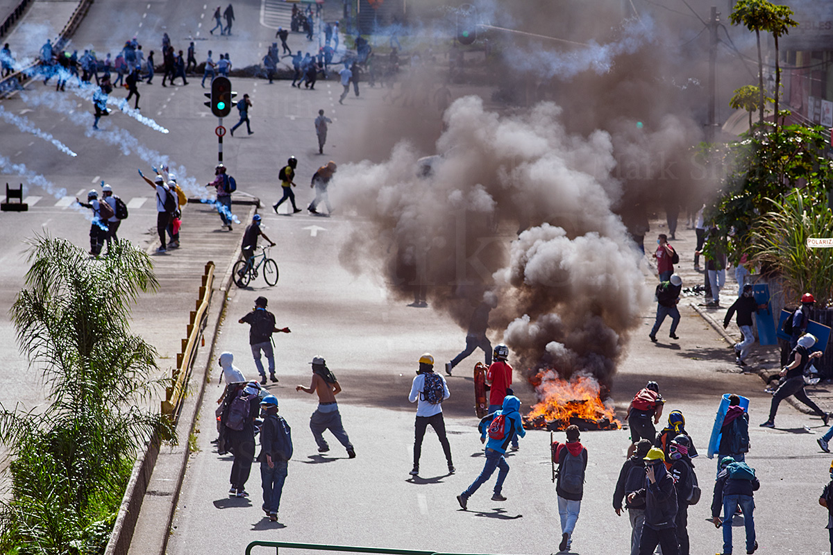 Burning barricade, protesters and tear gas cannisters flying in