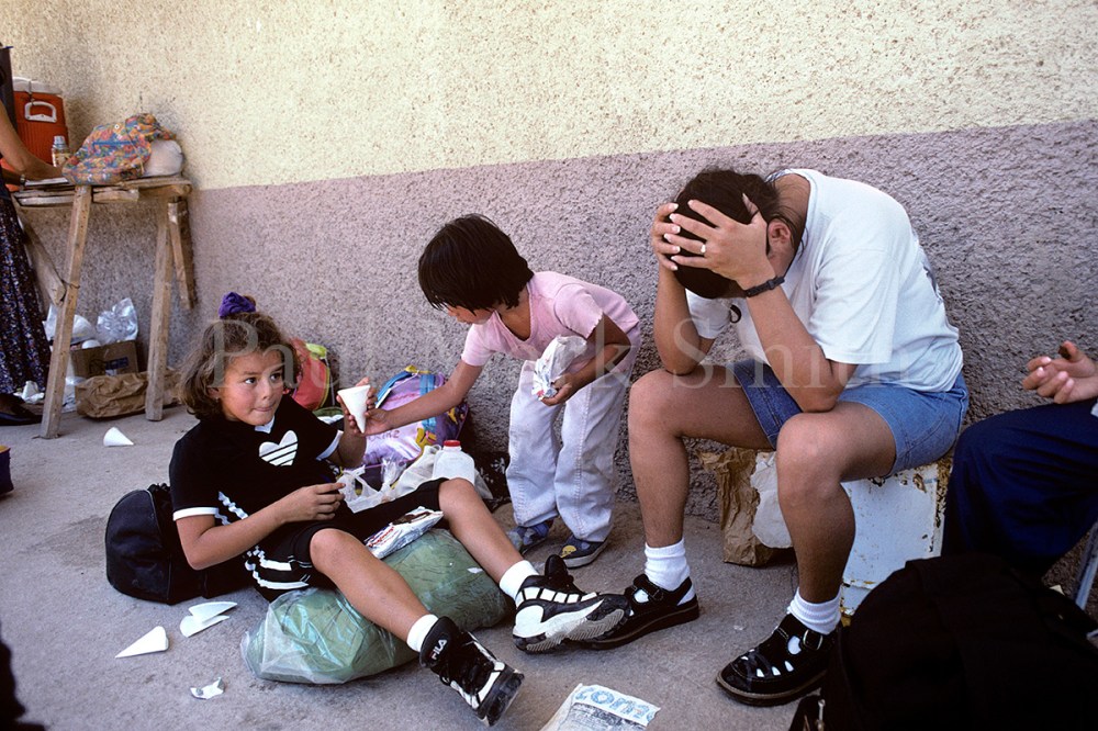 A deported migrant mother with her head in her hands as her children look on