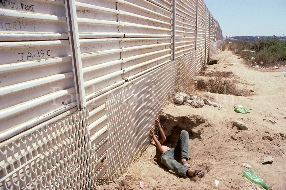 A migrant goes under the border fence between Tijuana and San Diego.